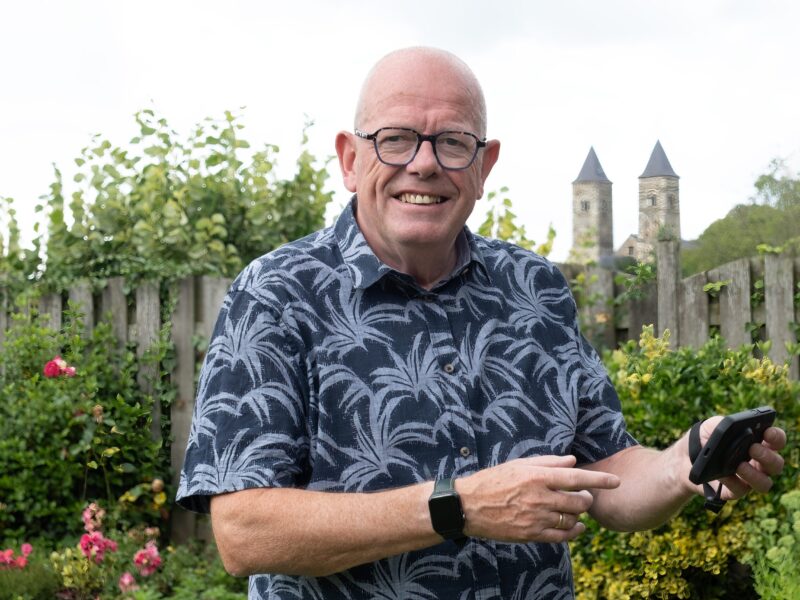 John Hillen in zijn tuin. Hij heeft een energiemeter in zijn hand.